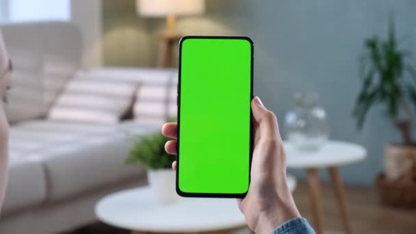 Primer plano de la mujer joven en casa sentada en una silla con un teléfono inteligente de pantalla falsa verde. Chica está viendo contenido sin tocar la pantalla del gadget. Modent Tecnología y Concepto de Información . — Vídeos de Stock