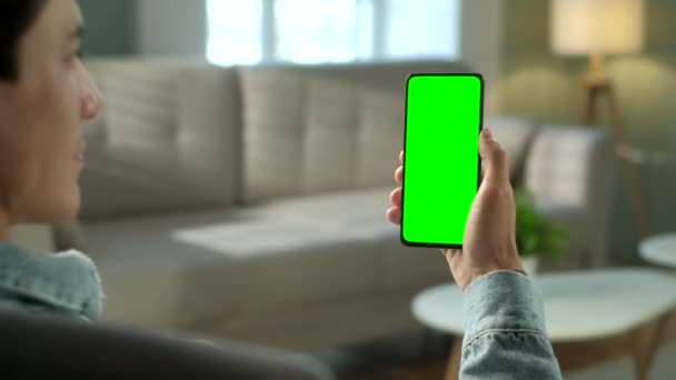 Vista posterior de la mujer en la habitación moderna sentada en una silla usando el teléfono con la llave verde del croma de la pantalla simulada sin los puntos de la pista que navegan el Internet que mira el contenido Videos Blogs. Desliza hacia arriba — Vídeos de Stock