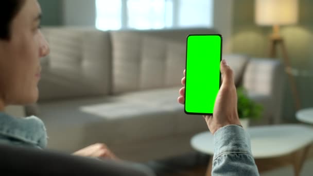 Vista posterior del hombre en el teléfono con pantalla verde para copiar el espacio. Chromakey se burlan sin rastrear marcadores. Veinte años Boy viendo el vídeo de noticias en el sofá de cerca. Pulse para hacer clic en Centro de pantalla — Vídeos de Stock