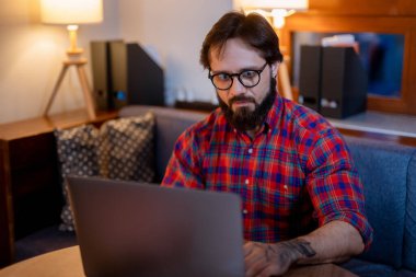 Gözlüklü ve tişörtlü yakışıklı bir adam boş karanlık ofiste dizüstü bilgisayarla masada oturuyor..
