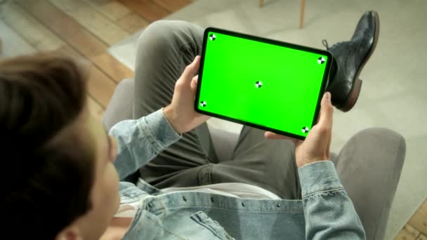 Вид с плеча человека, держащего в руках зеленый макбук-экран и сидящего на волоске. Мужчина покупает вещи или просматривает через Интернет . — стоковое видео