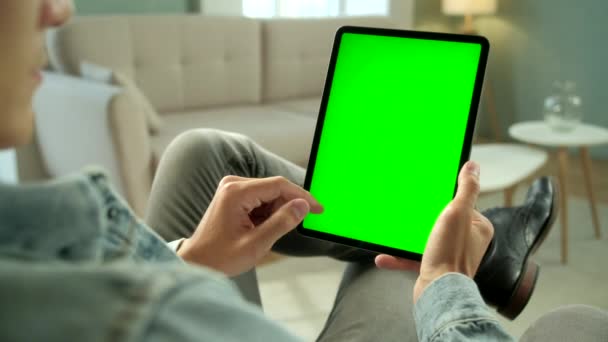 Vista desde el hombro del hombre sosteniendo y usando gestos de mano en la pantalla falsa verde Tableta digital Ordenador sentado en una silla. Hombre Comprar cosas o navegar a través de Internet . — Vídeos de Stock