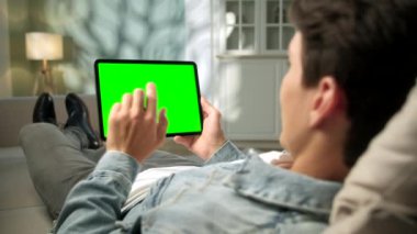 Green Mock-up Ekran Dijital Tableti Bilgisayarında Koltuğun Üzerinde Uzanırken İnsan Omuzundan Görünüm. Arka plandaki rahat oturma odasında. Orta Ekranda Tıklama