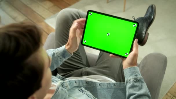 Vista dalla spalla dell'uomo che tiene e usa i gesti della mano sullo schermo verde simulato Tablet digitale seduto su una sedia. Comprare roba maschile o Browsing. Toccando sullo schermo centrale — Video Stock