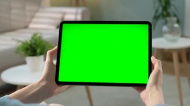 Bakış açısı: Evde oturan genç kadın yeşil maket tabletini kullanarak sandalyeye oturuyor. Dokunmatik Ekran Aygıtı Kullanan Kız, İnternet Taraması. Yeşil Ekran ve Krom Anahtarı Konsepti.