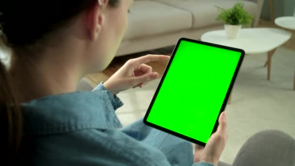 从坐在椅子上的绿色模拟屏幕数字平板电脑上的女性手持和使用手持设备的肩膀看问题。买东西或上网的女孩. — 图库视频影像
