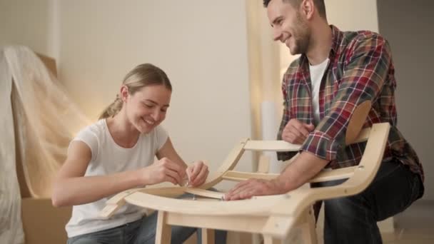 Adultos jóvenes mudándose a un nuevo hogar. Pareja moviéndose en el montaje de muebles de silla. Joven pareja interracial en un nuevo hogar. reparación, renovación y concepto de personas — Vídeos de Stock