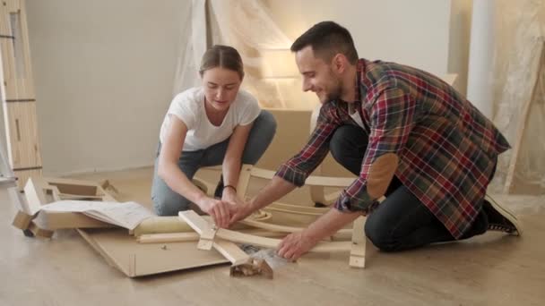 Young adults moving in new home. Couple moving in assembling chair furniture. Young interracial couple in new home. repair, renovation and people concept — Stock Video