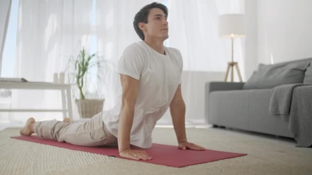 Joven Hombre Deportivo en Ropa Deportiva haciendo Ejercicios de Yoga. Masculino practicando hacia abajo frente a la postura del perro en el ejercicio deportivo de yoga en casa. Inicio Entrenamiento, Formación y Bienestar Concepto . — Vídeos de Stock