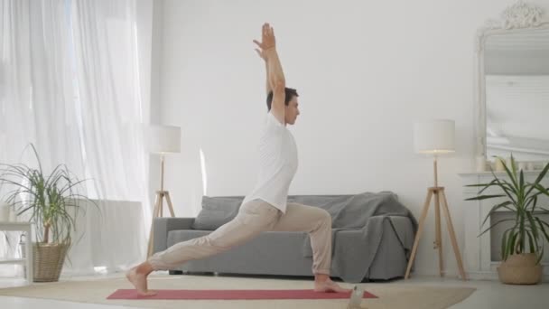 Man Practice Warrior Yoga Pose στο σαλόνι. Αθλητικός άνθρωπος κάνει γιόγκα για τη φροντίδα του σώματος, υγιή σπονδυλική στήλη και παραγωγική ημέρα — Αρχείο Βίντεο