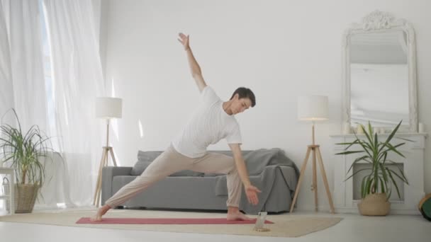 Людина практикує воїн йогу позу у вітальні. Спортивний чоловік робить йогу для догляду за тілом, здорового спинного мозку й продуктивного дня — стокове відео