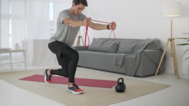 Direniş Bandosu ile Genç Sporcu Egzersizleri. Jimnastik eğitmeni, pencereli beyaz bir arka plan duvarında lastik bantlı esneme hareketleri yapıyor. Evde Kalma Konsepti.