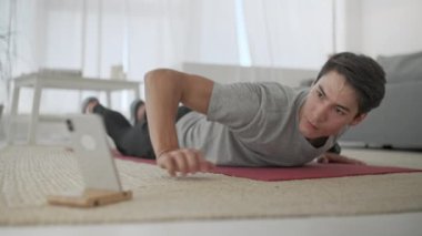 Gri tişörtlü yakışıklı genç adam ve siyah şortlu adam internette spor yapıyor. Yakışıklı Adam Evdeki Oturma Odasında Egzersiz Yapıyor ve şınav çekiyor.