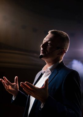 Karanlık konferans salonunda mikrofonla konuşan adamların portresi. Kapalı alandaki üniversite öğrencilerine başarılı satışlar için pazarlama ve yönetimden bahsediyor. Profesyonel fikirler, politika