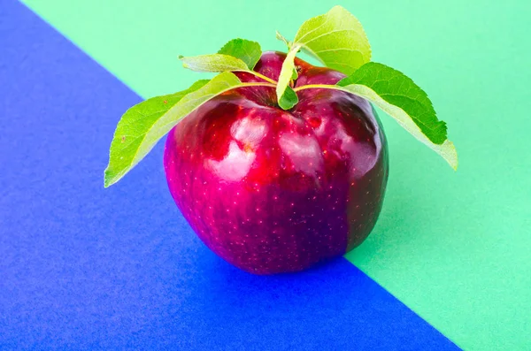 Single red ripe sweet apple with green leaves