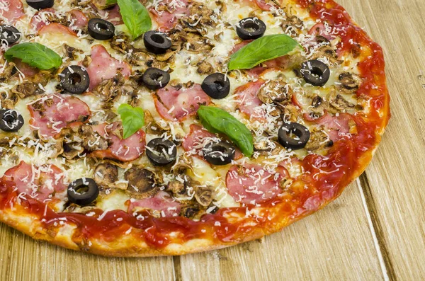 Pizza com presunto, cogumelos e azeitonas na superfície de madeira . — Fotografia de Stock