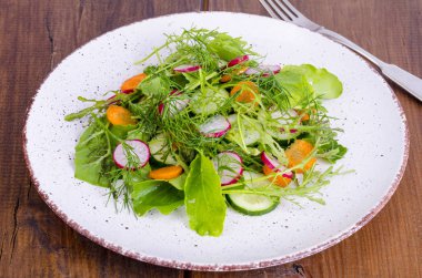 Beyaz tabakta taze sebze ve yeşil salata yaprakları