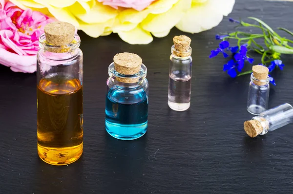 Trois bouteilles d'huile essentielle avec des fleurs fraîches sur fond noir — Photo