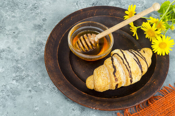 Fresh croissant, honey, yellow flowers.