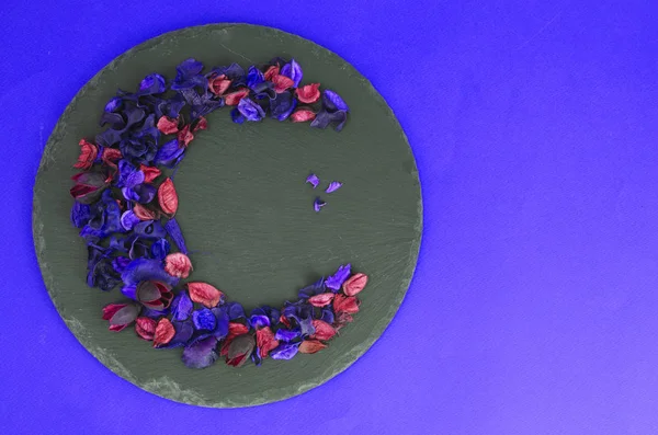 Creative flower composition in form of crescent of dry flowers and petals, green leaves. Top view, flat lay.
