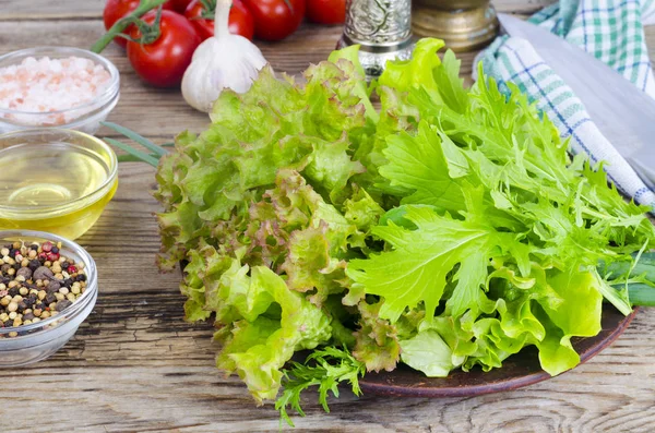 Green salad ingredients organic lettuce, cherry tomatoes, spices and olive oil on wooden background.