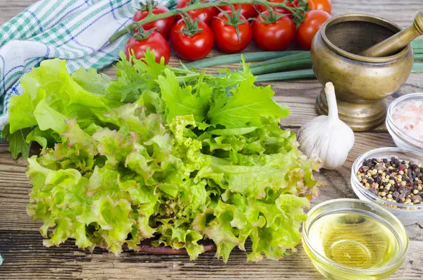 Green salad ingredients organic lettuce, cherry tomatoes, spices and olive oil on wooden background.