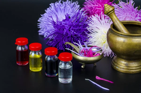 Glass bottles of essential oil with fresh flowers on black background. — Stock Photo, Image