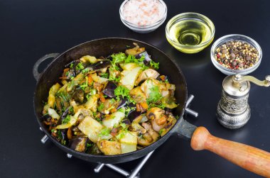 Siyah arka plan üzerinde tavada kızarmış patlıcan, kırmızı biber ve farklı sebzeler