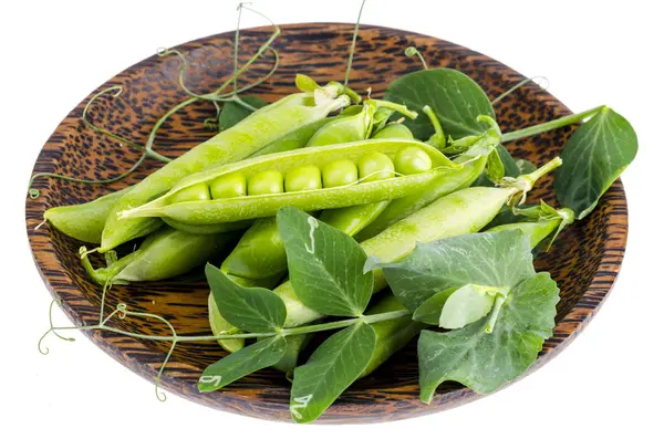 白い上に緑のエンドウ豆のポッドを持つ木製のプレート. — ストック写真