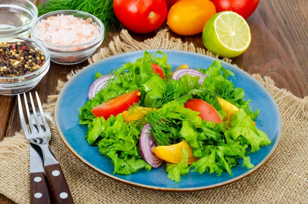 Leichte Mahlzeit aus grünen Salatblättern, gelben und roten Tomaten, Olivenöl auf Holztisch. — Stockfoto