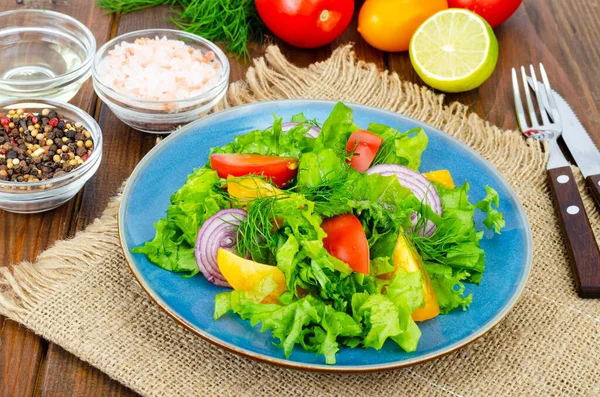 Leichte Mahlzeit aus grünen Salatblättern, gelben und roten Tomaten, Olivenöl auf Holztisch. — Stockfoto