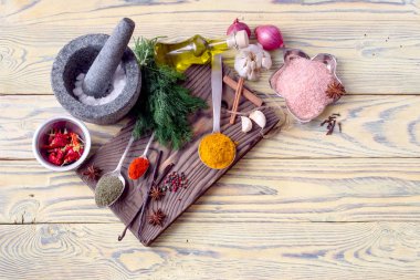 Çeşitli baharatlar, harç ve havaneli, zeytinyağında tabak ve kaşık ve mutfak otlar üzerinde sarı, ahşap masa yakın.