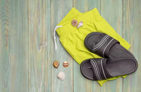 Men\'s beachwear and slippers and seashells on a wooden background close-up