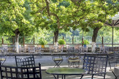 Metal masa ve sandalye bir sokak kafe-restoran güneşli yaz gününde (Tzoumerka, Epirus, Yunanistan büyük çınar ağaçlarının altında).