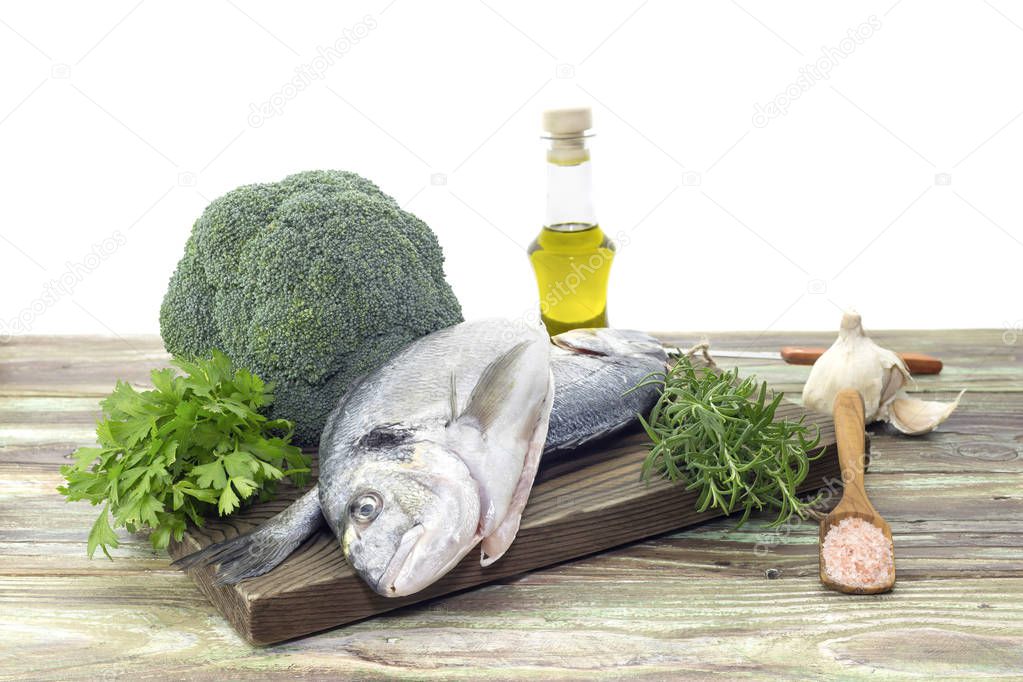 Fish sea breams(Sparus aurata) on a cutting board, olive oil, broccoli, garlic and aromatic herbs on a wooden table close-up.