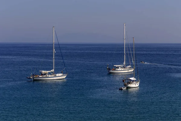 White yachts with sails moored in the open sea, near the shore on a summer, sunny day (region of Epirus, Greece).