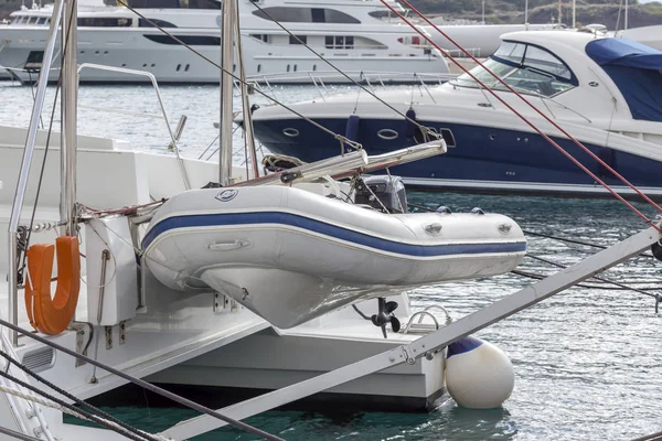 A white motor boat hangs on a moored yacht on a cloudy day close-up.