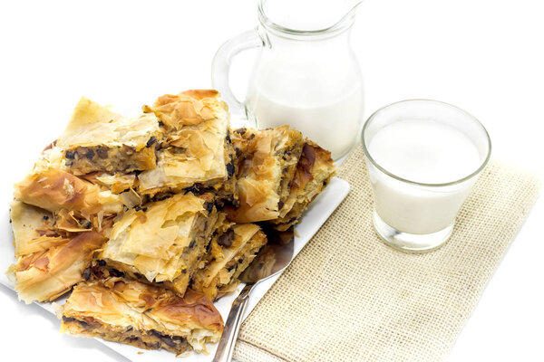 Ready meal. Milk in a jug and glassful, ruddy pies with potatoes and mushrooms lie on a plate close-up on a white background