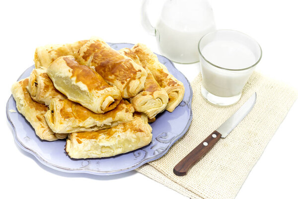 Ready meal. Milk in a jug and glassful, ruddy pies with cabbage and mushrooms lie on a plate close-up on a white background
