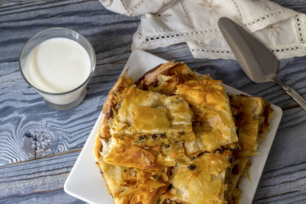 Ready meal. Milk in a jug and glassful, ruddy pies with potatoes and mushrooms lie on a plate close-up on a wooden table