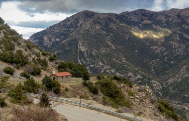 Küçük, beyaz, ortodoks bir Hıristiyan kilisesi dağlarda yol kenarında, bulutlu bir kış günü (Yunanistan, Mora))