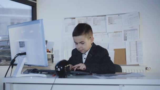 Маленький симпатичный мальчик, работающий с улыбкой за компьютером в офисе. 4K — стоковое видео