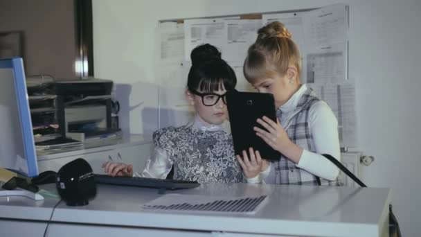 Zwei kleine Schulmädchen, die im Büro mit Tablets beraten. 4k — Stockvideo