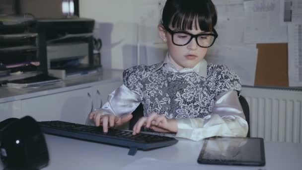 Маленькая девочка работает с компьютером и планшетом в офисе. 4K — стоковое видео