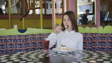 Mutlu kız tatlı yiyor, kameraya bakar ve 4 k kafede içecekler bir suyu