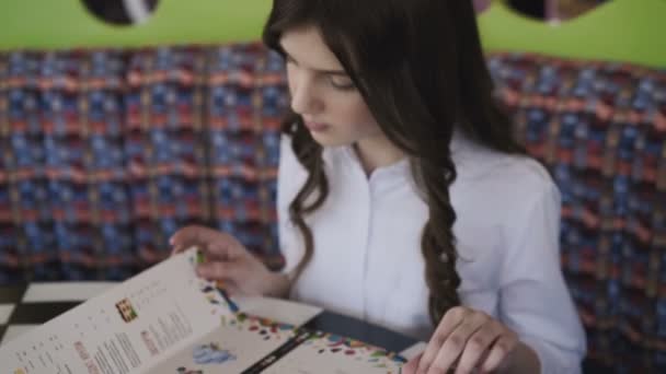 Bella, sorridente e giovane ragazza che legge il menu nel caffè. 4K — Video Stock