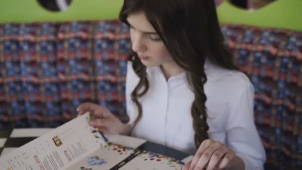 Chica bonita, sonriente y joven leyendo el menú en la cafetería. 4K — Vídeos de Stock