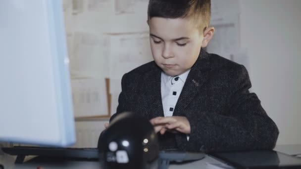 Серйозний красивий зайнятий хлопчик, що друкує на клавіатурі за столом — стокове відео