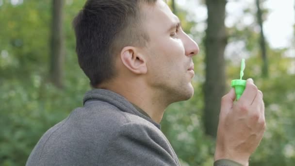 Porträt des gutaussehenden Vaters pustet Seifenblasen im Park. langsam — Stockvideo