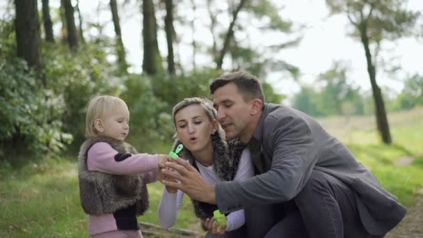 Щаслива сім'я відпочиває на природі з дитиною, дме і ловить бульбашки — стокове відео